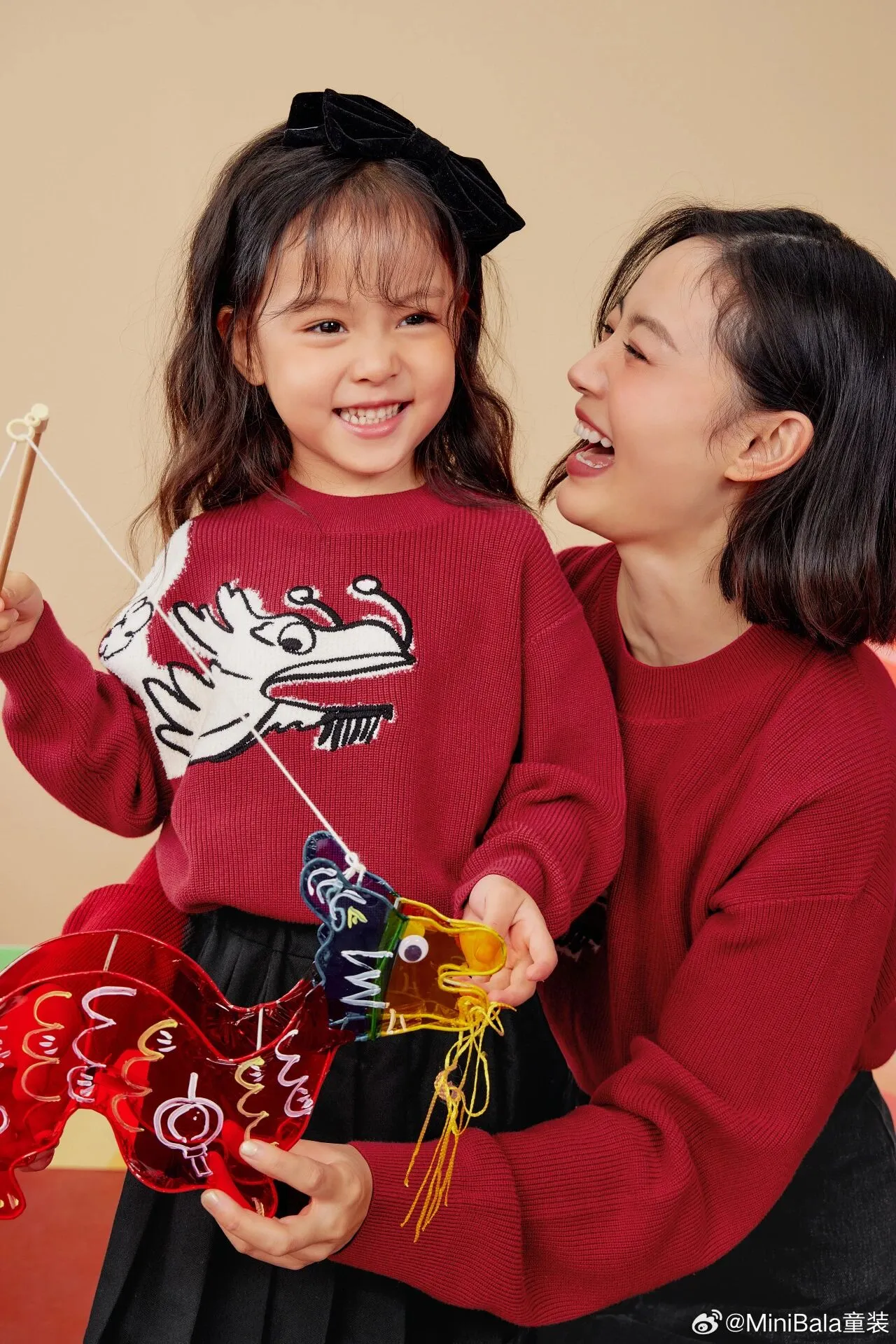 A child in a red dragon-motif jumper holds a small dragon prop beside an adult.